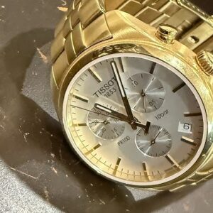 Tissot PR 100 Chronograph Gold, Damenuhr mit goldfarbenem Gehäuse, weißem Perlmutt-Zifferblatt und Chronographenfunktion. | Zustand: Gut