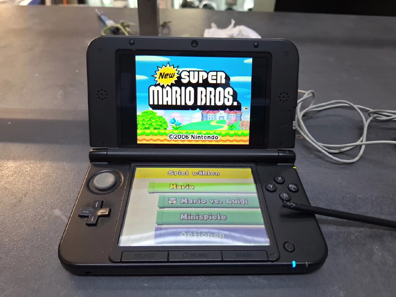 Nintendo 3DS XL Schwarz Silber, Handheld-Konsole inkl. Ladekabel und dem Spiel New Super Mario Bros., Gehäuse an der rechten Ecke gebrochen. | Zustand: In Ordnung | Farbe: schwarz – Bild 2